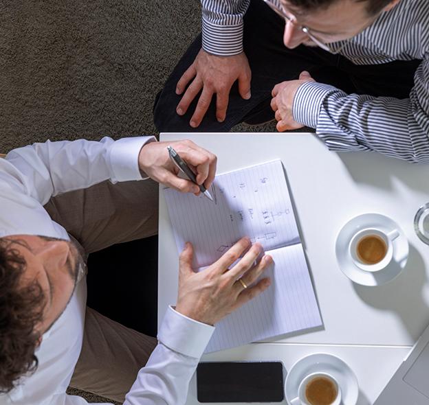 Two people at a table with a sketch on a notepad between them.